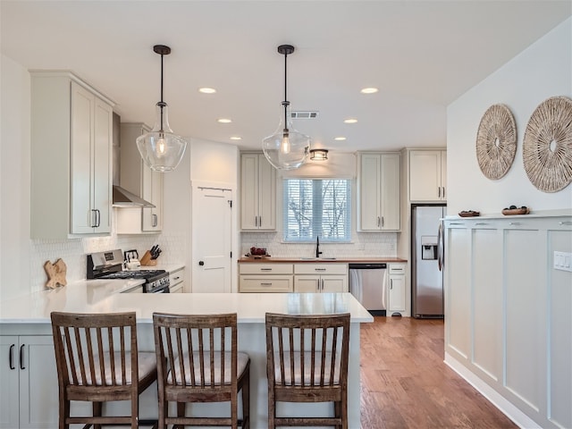 kitchen with stainless steel appliances, wall chimney range hood, dark hardwood / wood-style floors, pendant lighting, and a breakfast bar area