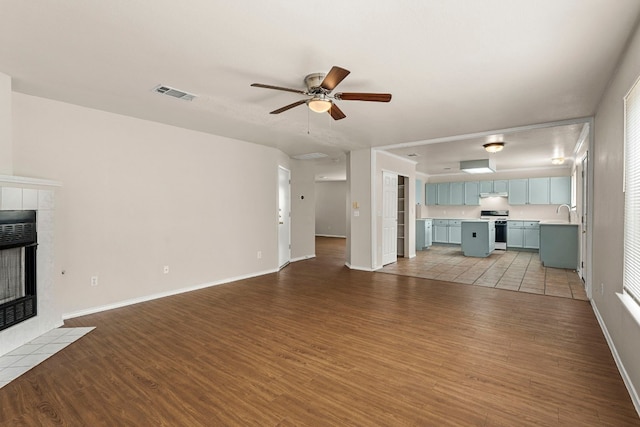 unfurnished living room with hardwood / wood-style floors, ceiling fan, and a tile fireplace