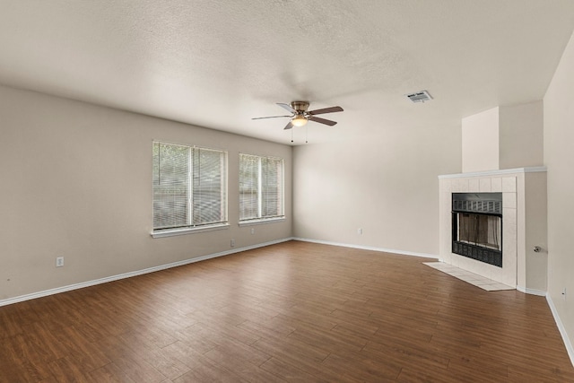 unfurnished living room with ceiling fan, a tile fireplace, dark hardwood / wood-style flooring, and a textured ceiling