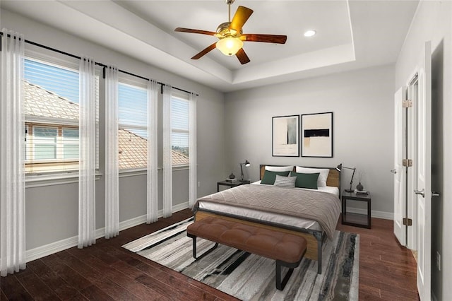 bedroom featuring dark hardwood / wood-style flooring, ceiling fan, a tray ceiling, and multiple windows