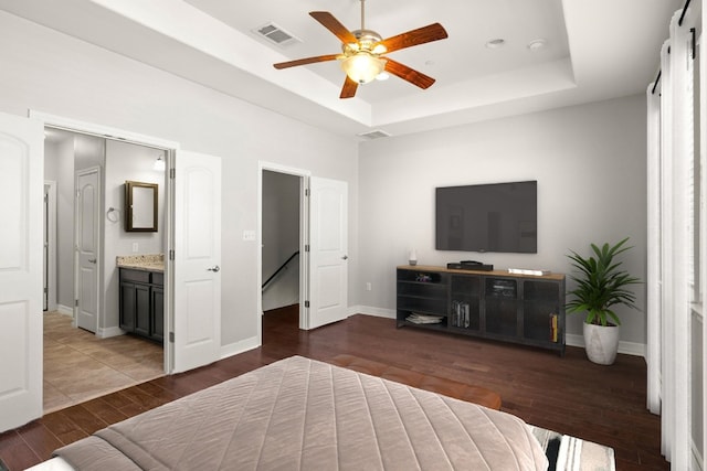 bedroom with dark wood-type flooring, a tray ceiling, ceiling fan, and connected bathroom