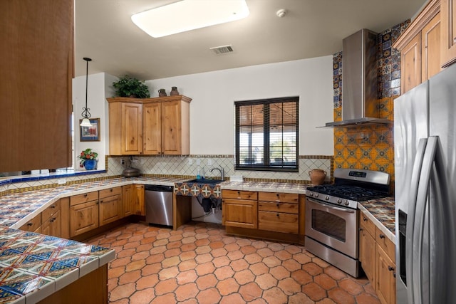 kitchen featuring tasteful backsplash, tile countertops, stainless steel appliances, hanging light fixtures, and wall chimney exhaust hood