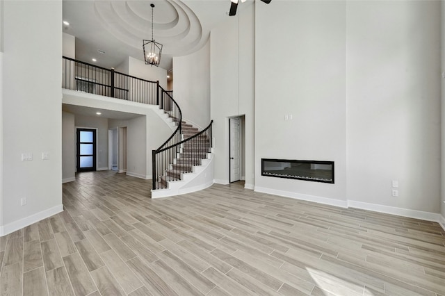 unfurnished living room featuring a towering ceiling, an inviting chandelier, and light hardwood / wood-style flooring