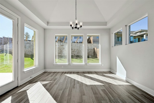 unfurnished dining area featuring wood-type flooring, an inviting chandelier, a raised ceiling, and lofted ceiling