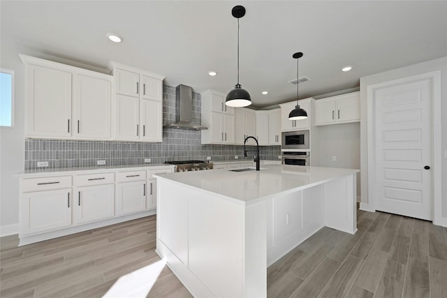 kitchen with a kitchen island with sink, sink, wall chimney exhaust hood, white cabinetry, and stainless steel appliances