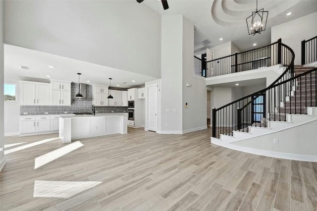 unfurnished living room featuring a towering ceiling, an inviting chandelier, light hardwood / wood-style flooring, and sink