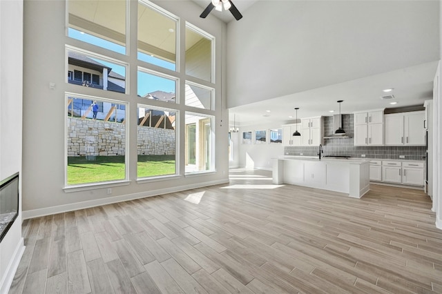 unfurnished living room with ceiling fan, a towering ceiling, sink, and light hardwood / wood-style flooring