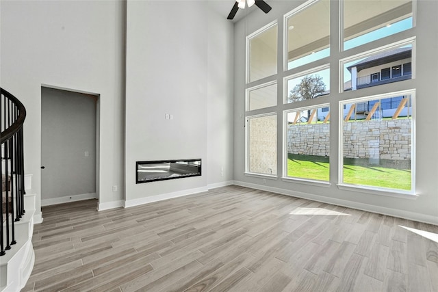 unfurnished living room with ceiling fan, light hardwood / wood-style flooring, and a towering ceiling