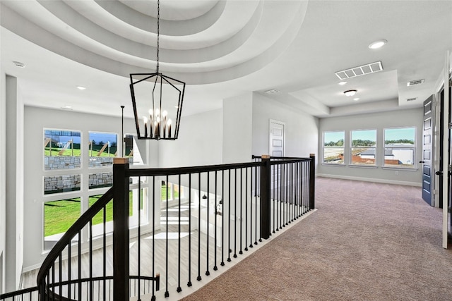 hall with carpet flooring, a tray ceiling, and an inviting chandelier