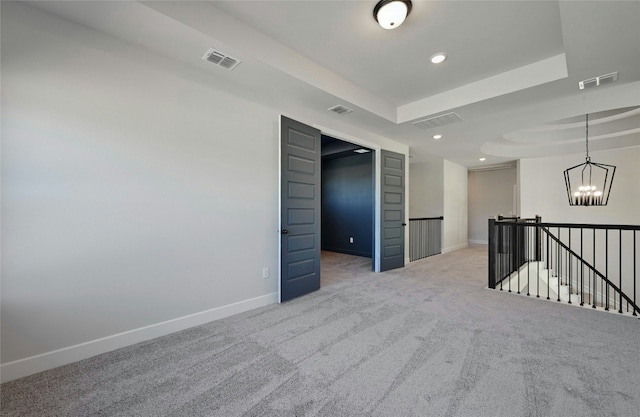 spare room featuring a tray ceiling, light colored carpet, and an inviting chandelier