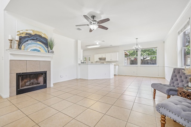 living room with ceiling fan with notable chandelier, a tiled fireplace, light tile patterned floors, and crown molding