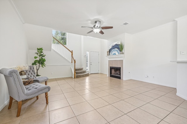 tiled living room featuring a tile fireplace, ornamental molding, and ceiling fan