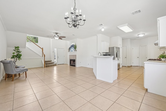 kitchen with white cabinetry, a tile fireplace, ceiling fan with notable chandelier, light tile patterned floors, and pendant lighting