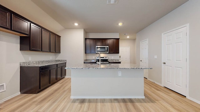 kitchen with light stone countertops, light hardwood / wood-style flooring, stainless steel appliances, and an island with sink