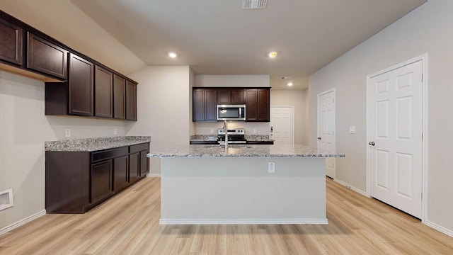 kitchen with dark brown cabinetry, light wood-style floors, light stone countertops, and stainless steel appliances