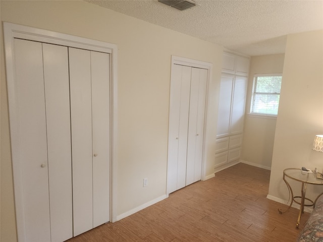 unfurnished bedroom with multiple closets, a textured ceiling, and light wood-type flooring