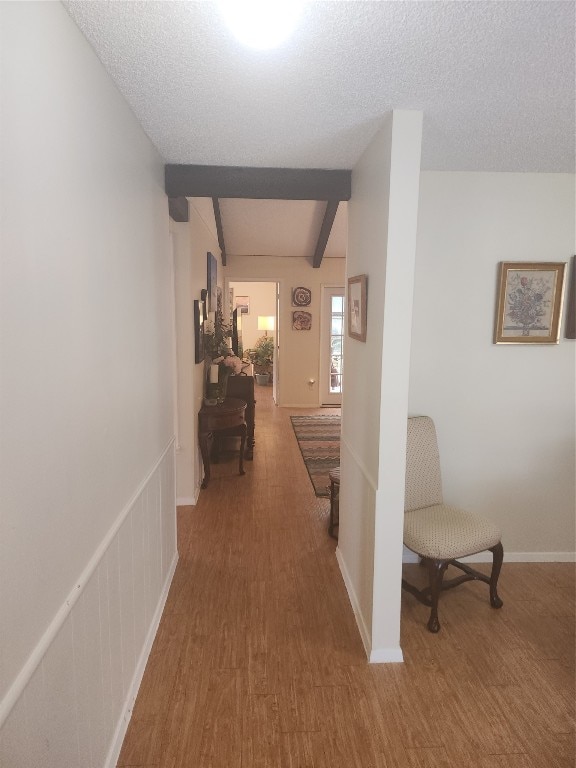 corridor with beamed ceiling, a textured ceiling, and wood-type flooring