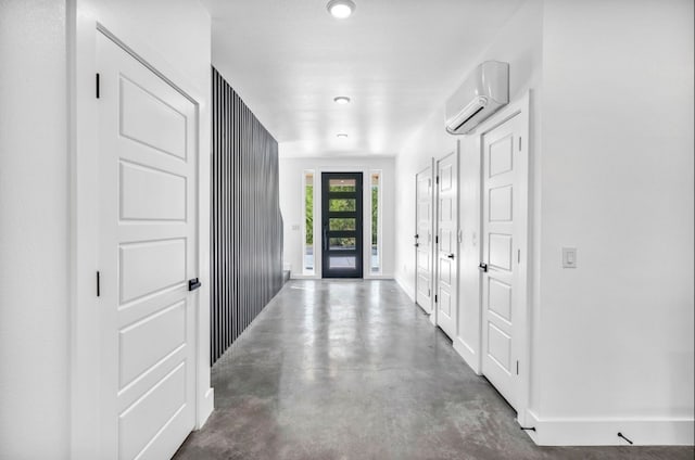 hall with concrete flooring, a wall mounted air conditioner, and baseboards