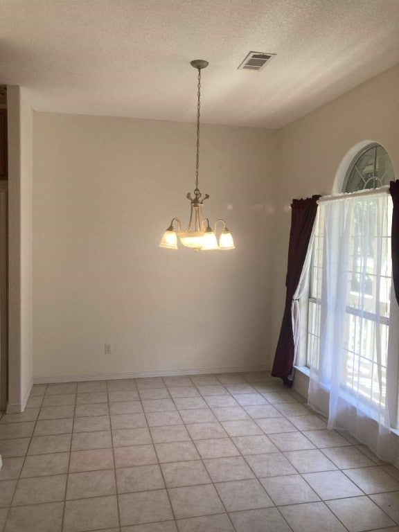 tiled spare room featuring a chandelier and a textured ceiling