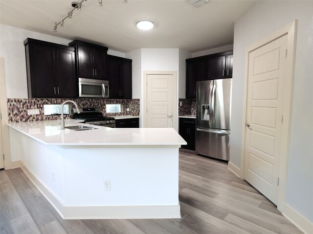 kitchen featuring sink, kitchen peninsula, tasteful backsplash, appliances with stainless steel finishes, and light hardwood / wood-style floors