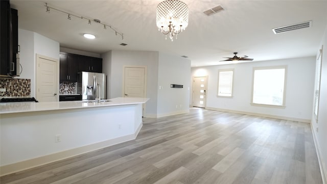 kitchen featuring stainless steel fridge, decorative backsplash, ceiling fan with notable chandelier, light wood-type flooring, and sink