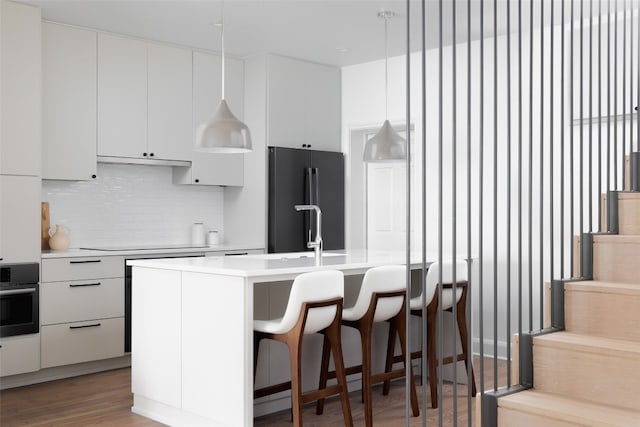 kitchen with a center island with sink, oven, white cabinets, hanging light fixtures, and high quality fridge