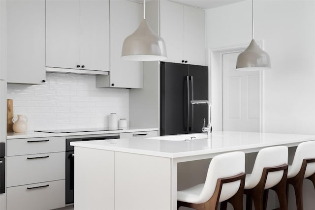 kitchen with decorative backsplash, a breakfast bar area, under cabinet range hood, light countertops, and black appliances