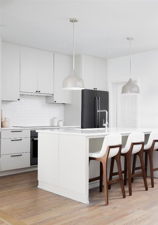 kitchen featuring white cabinetry, high quality fridge, pendant lighting, and a kitchen island with sink