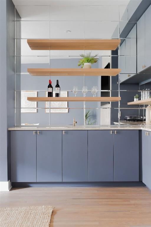 bar featuring blue cabinetry, backsplash, and light wood-type flooring