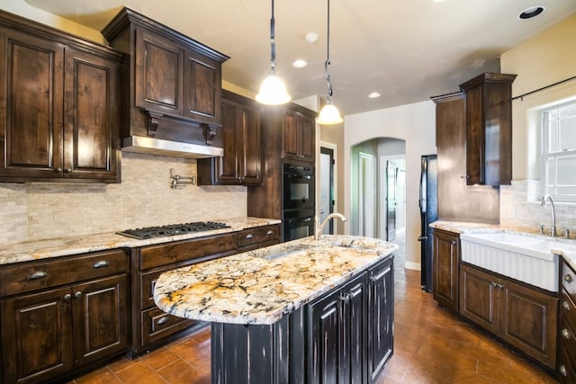 kitchen featuring a kitchen island, light stone countertops, black appliances, backsplash, and sink