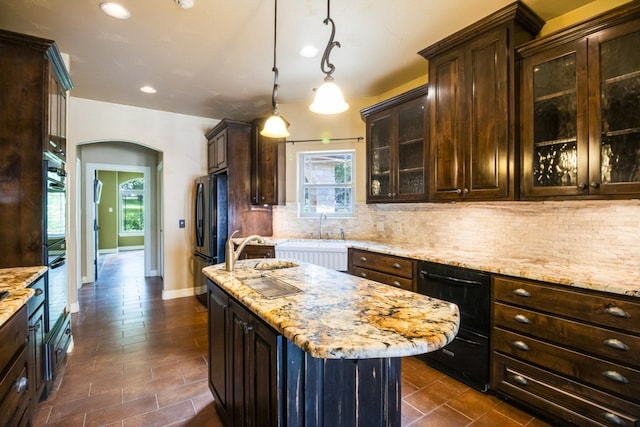 kitchen with black appliances, light stone counters, dark brown cabinets, and an island with sink