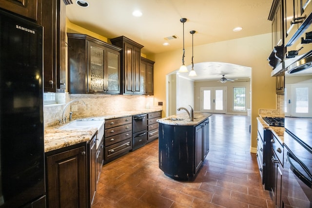 kitchen with light stone countertops, sink, black fridge, ceiling fan, and a kitchen island with sink