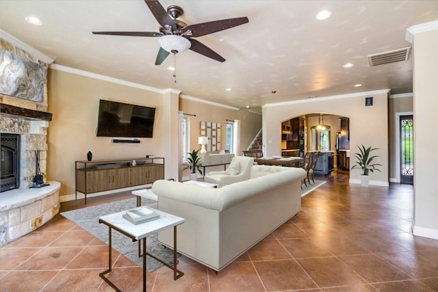 living room featuring a fireplace, ornamental molding, ceiling fan, and tile patterned floors