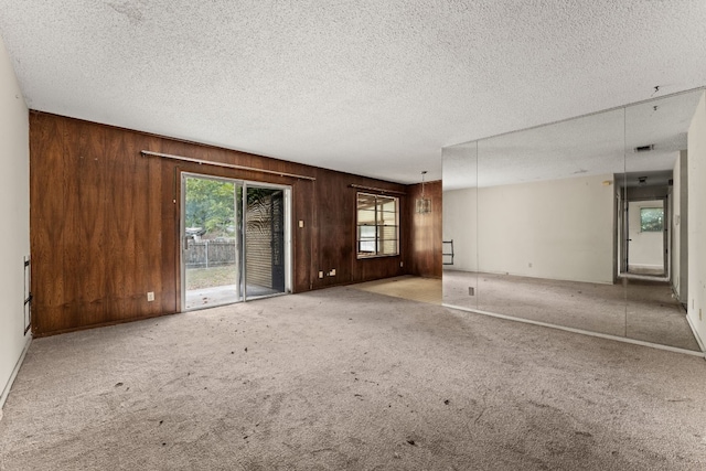 unfurnished living room featuring a textured ceiling, carpet, and wood walls