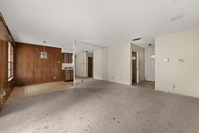 unfurnished living room with wooden walls, an inviting chandelier, and a textured ceiling