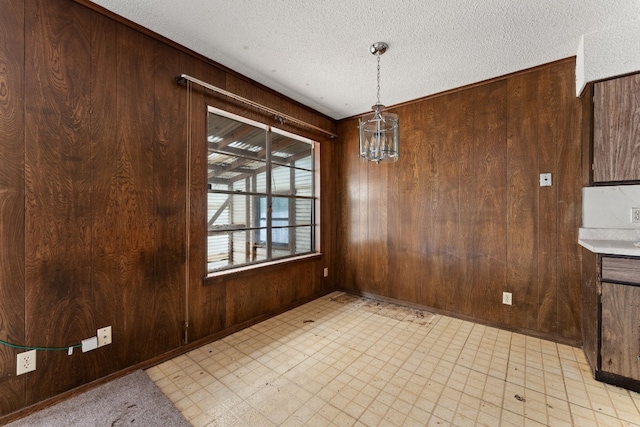 unfurnished dining area with wood walls, a chandelier, and a textured ceiling