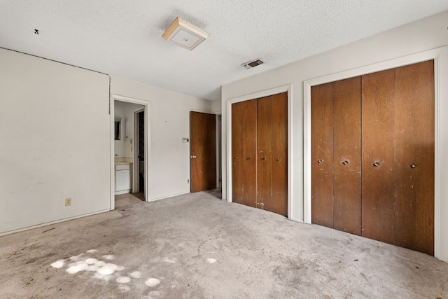 unfurnished bedroom featuring a textured ceiling, two closets, ensuite bathroom, and carpet floors