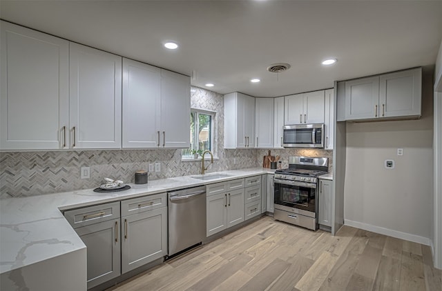 kitchen with backsplash, light stone counters, stainless steel appliances, light hardwood / wood-style floors, and sink