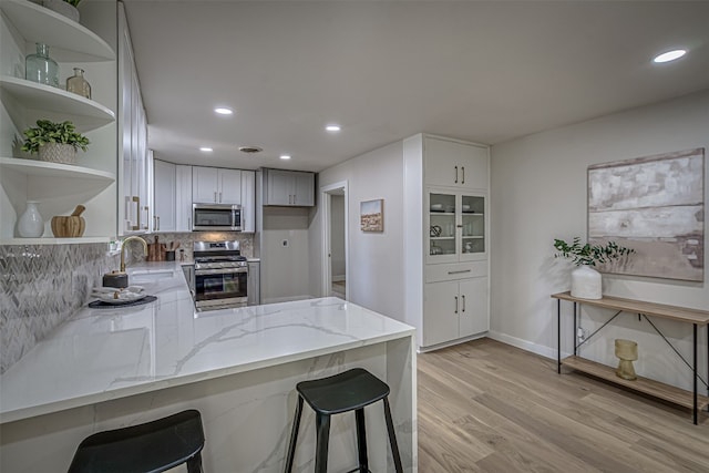 kitchen featuring light wood-type flooring, appliances with stainless steel finishes, light stone counters, kitchen peninsula, and decorative backsplash