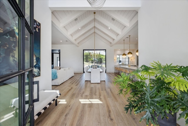 interior space with an inviting chandelier, beam ceiling, light hardwood / wood-style flooring, and high vaulted ceiling