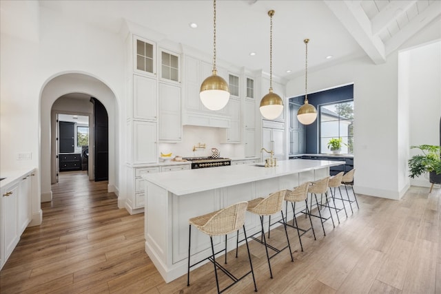 kitchen featuring light wood-type flooring, a kitchen breakfast bar, an island with sink, and white cabinets