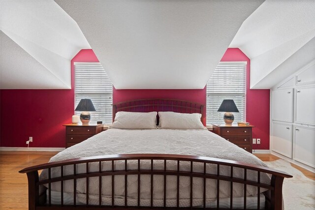 bedroom with multiple windows, lofted ceiling, and light hardwood / wood-style floors