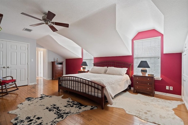 bedroom featuring ceiling fan, lofted ceiling, a textured ceiling, and light hardwood / wood-style flooring