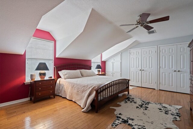 bedroom featuring vaulted ceiling, two closets, a textured ceiling, and light wood-type flooring