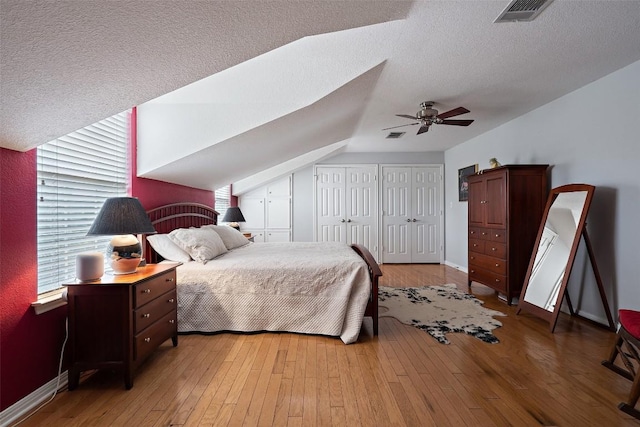 bedroom featuring hardwood / wood-style flooring, lofted ceiling, a textured ceiling, and two closets