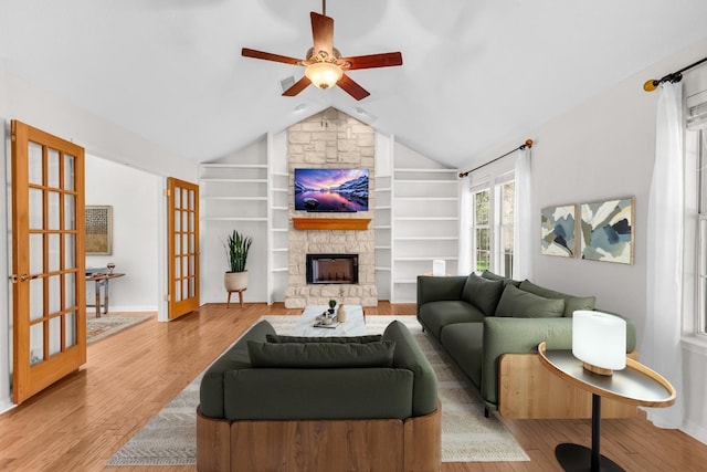 living room with a fireplace, lofted ceiling, ceiling fan, light wood-type flooring, and french doors