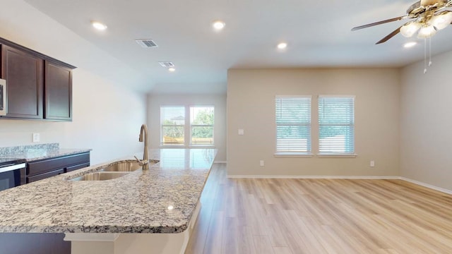 kitchen featuring light hardwood / wood-style floors, sink, light stone counters, and a center island with sink