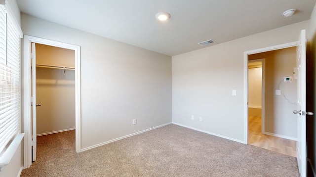 unfurnished bedroom with a closet, light carpet, and a walk in closet