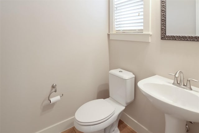 half bathroom with baseboards, a sink, and toilet