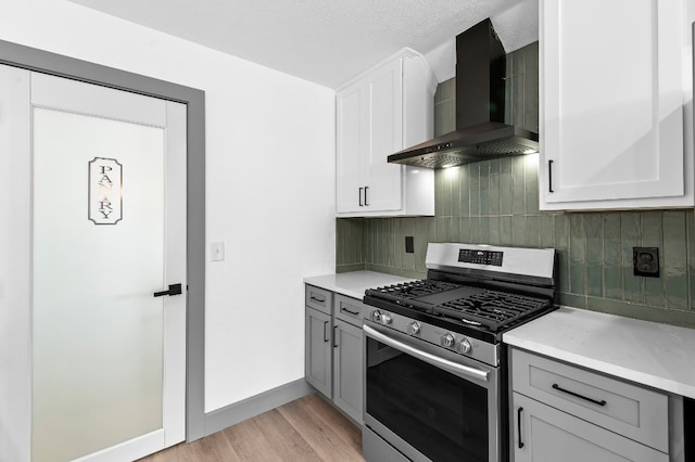 kitchen featuring tasteful backsplash, white cabinets, wall chimney range hood, light hardwood / wood-style flooring, and stainless steel gas stove